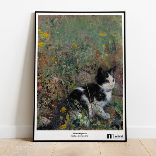 Poster med katt på blomsteräng i svart ram lutad mot en vägg