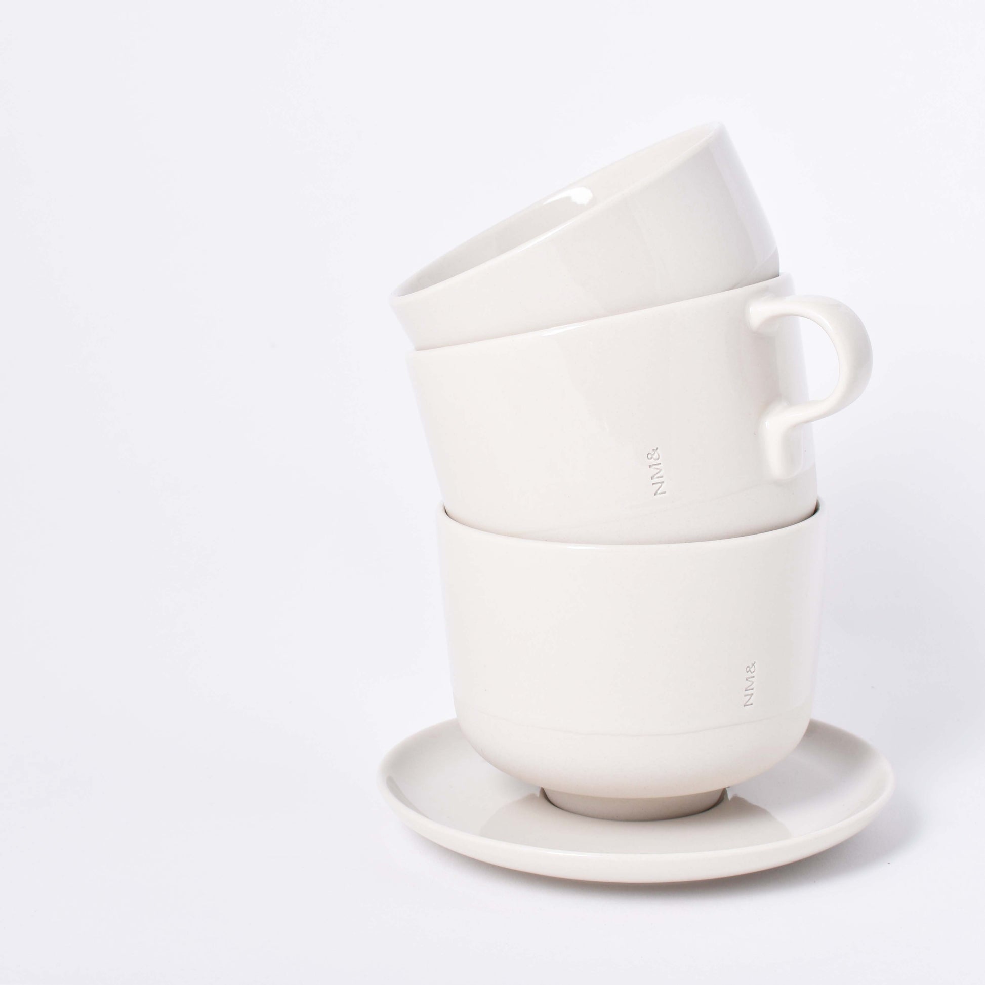 Tre sandfärgade koppar staplade på ett runt fat med NM& monogram ingraverat  i design av Carina Seth Andersson